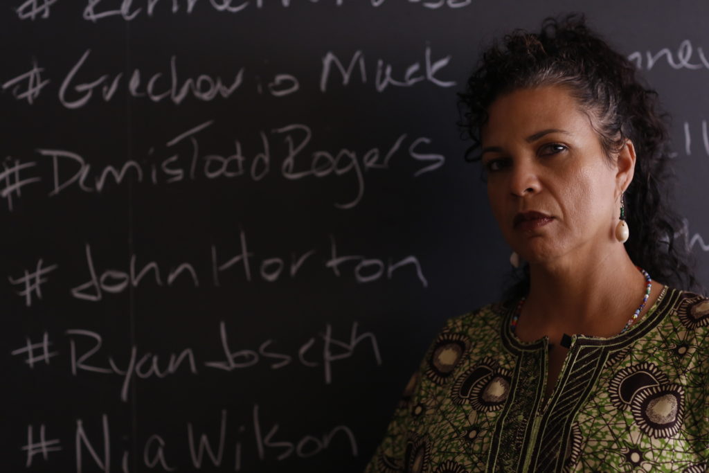 Melina Abdullah stands in front of a chalkboard displaying the names of people killed in police shootings.